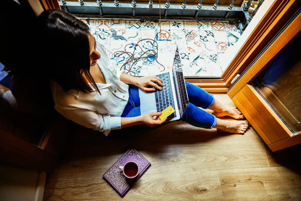 Mujer sentada en el suelo de una casa tomando café y usando portatil