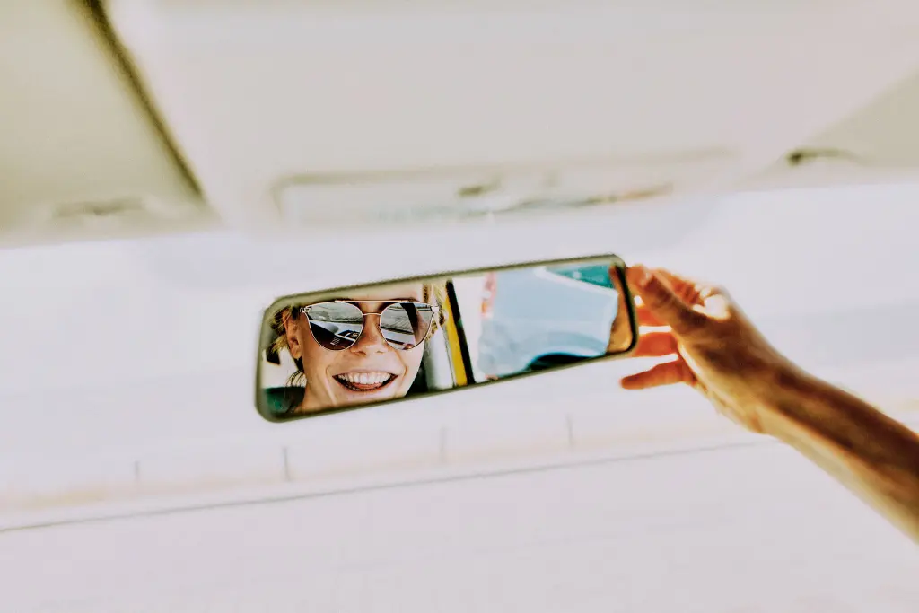 Chica con gafas de sol mirándose en el retrovisor.